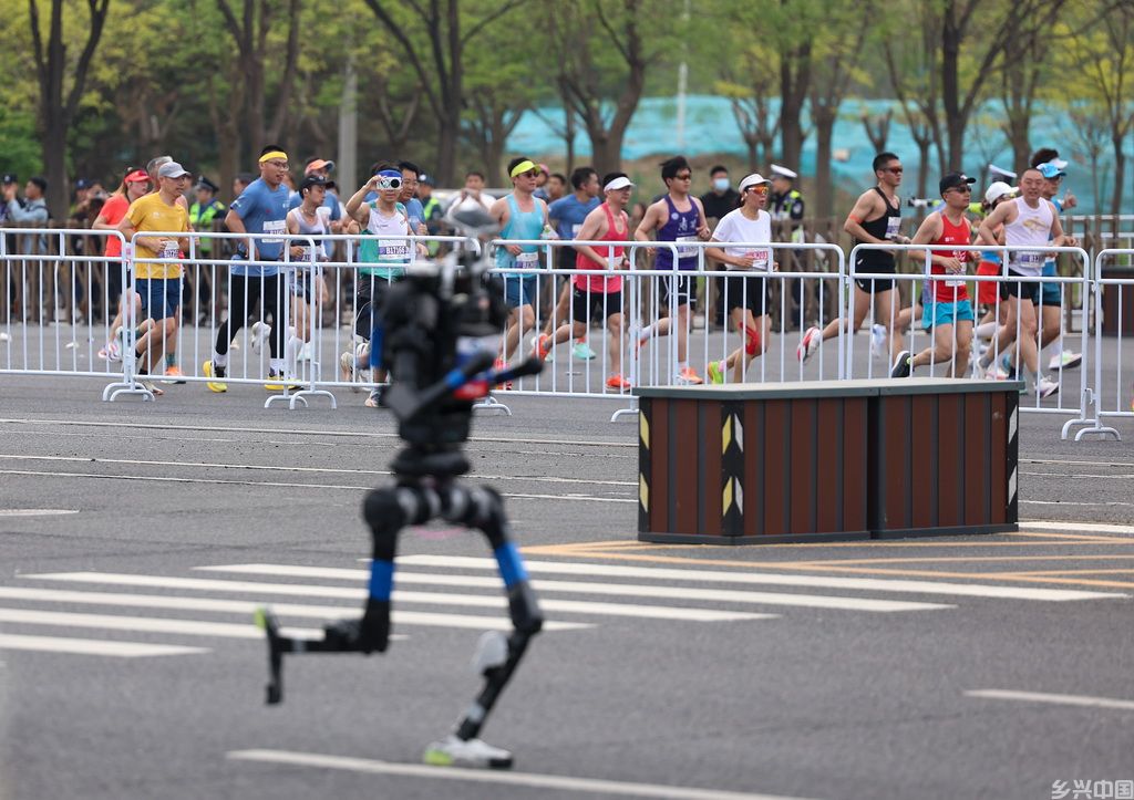 4月19日，参赛的长跑选手与杭U赛队自主人形机器人选手宇树H1（前）在比赛中。新华社记者 翟一凡 摄